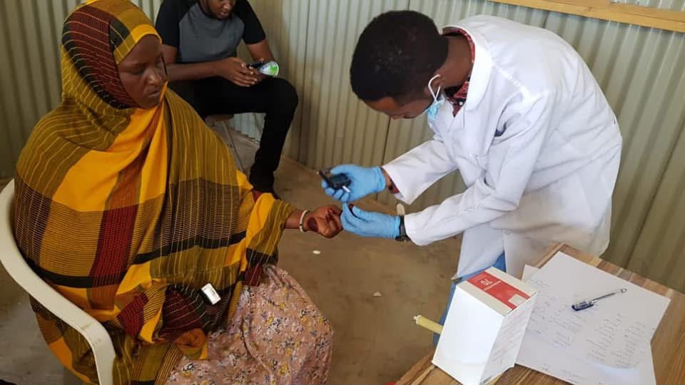 HDC outreach team performing a finger-prick glucose test on a patient