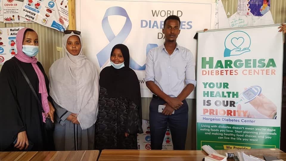 HDC team at a World Diabetes Day outreach, standing beside the HDC roll-up banner